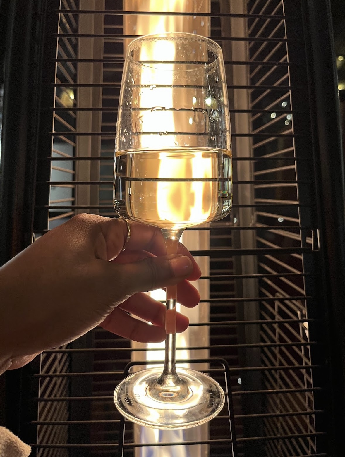 A glass of chilled white wine held up against the warm glow of a patio heater
