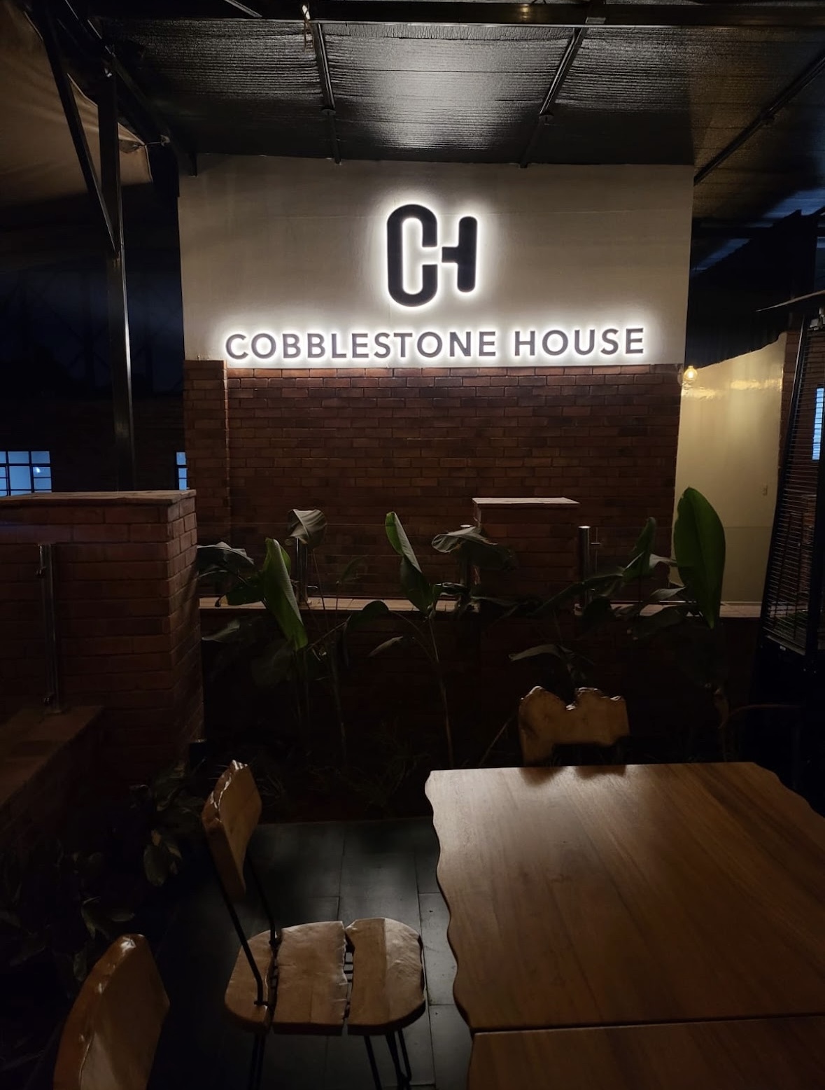 Illuminated Cobblestone House signage glowing above a brick wall and intimate evening seating